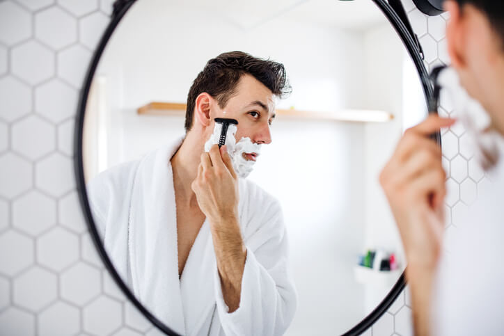 Young man shaving in the bathroom in front of a mirror